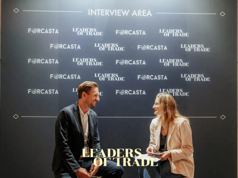 Two people in front of an event interview wall with sponsor logos